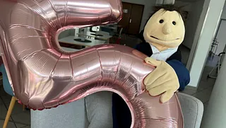 Die Handpuppe Käthe von Bora hält eine große, rosa Lufballon 5 in der Hand.